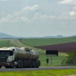 Caminhão de carga trafega por uma rodovia cercada por áreas agrícolas.