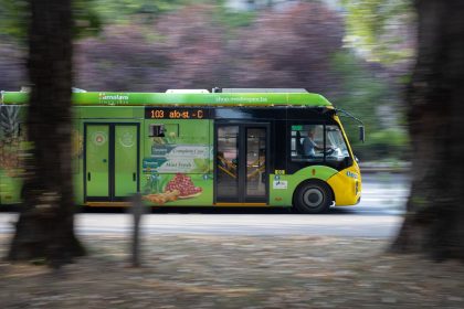 Ônibus elétrico verde circula por uma avenida movimentada de Sarajevo, entre carros e edifícios urbanos.