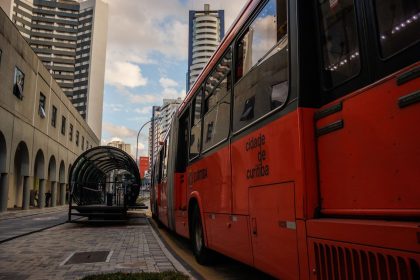 Ônibus urbano vermelho parado em uma estação moderna no centro de Curitiba.