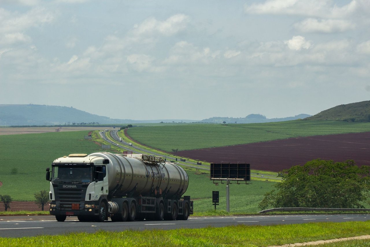 Caminhão de carga trafega por uma rodovia cercada por áreas agrícolas.